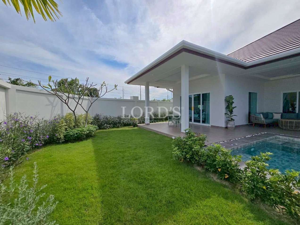 Private garden with manicured lawn, covered terrace, and swimming pool beside a modern villa.