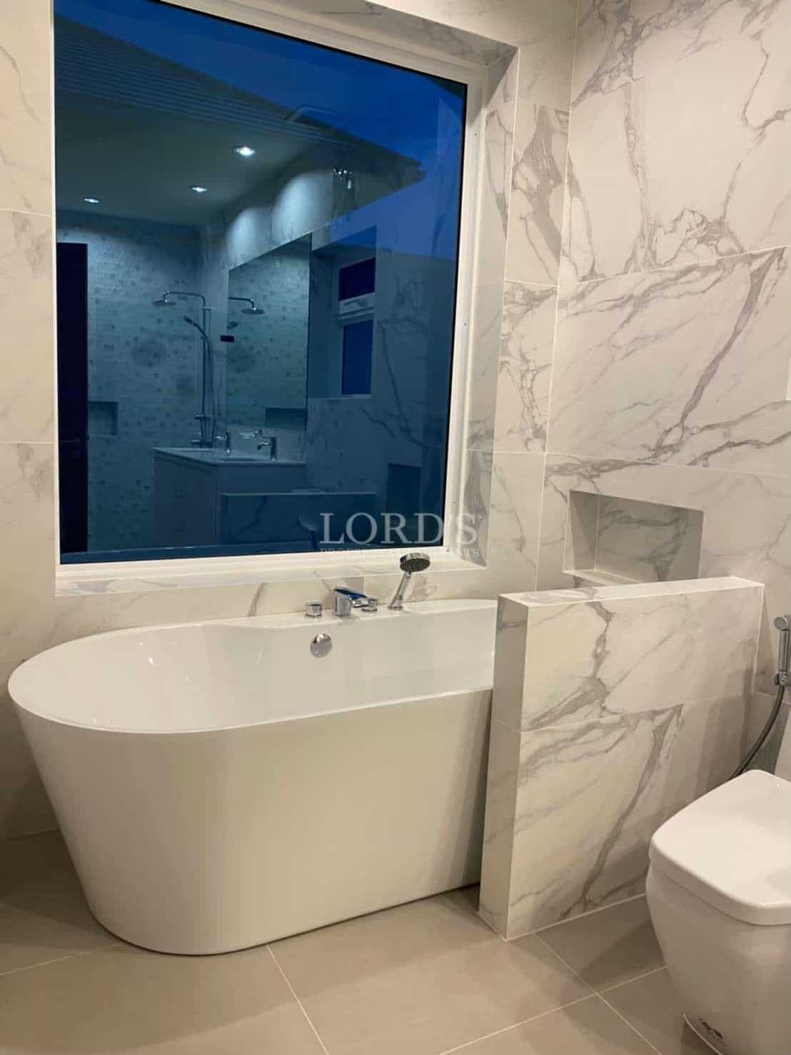 Luxury bathroom with freestanding bathtub, marble-look wall tiles, built-in niche, and modern fixtures.