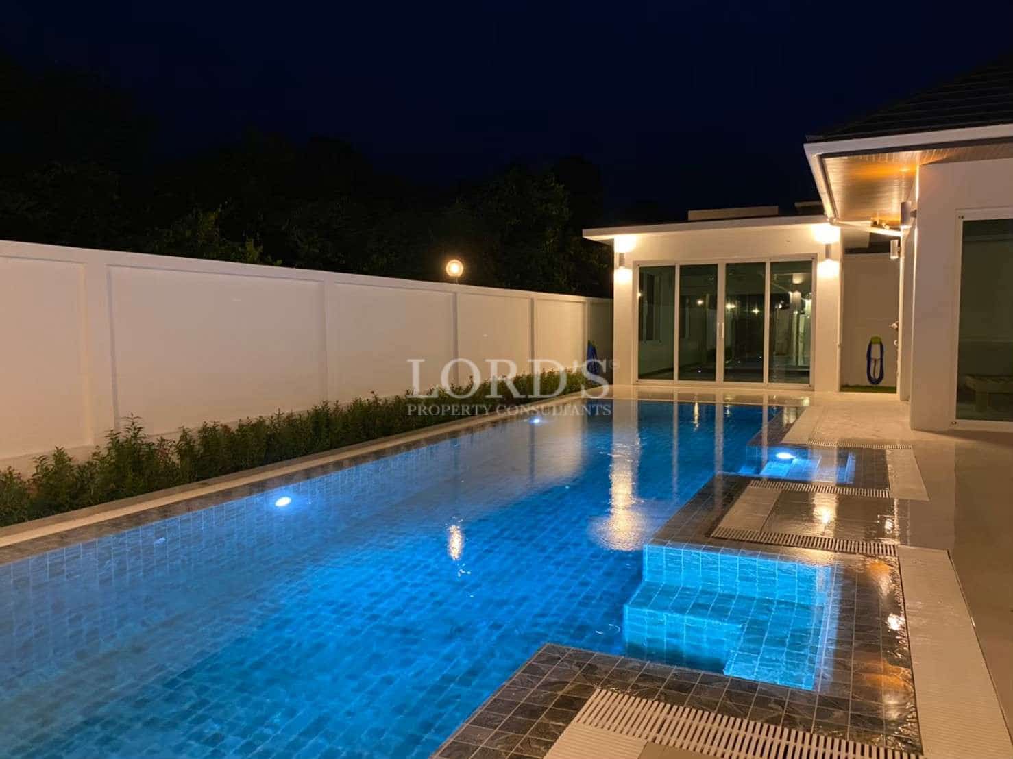 Private swimming pool at night with blue underwater lighting, modern villa exterior, and illuminated poolside terrace.