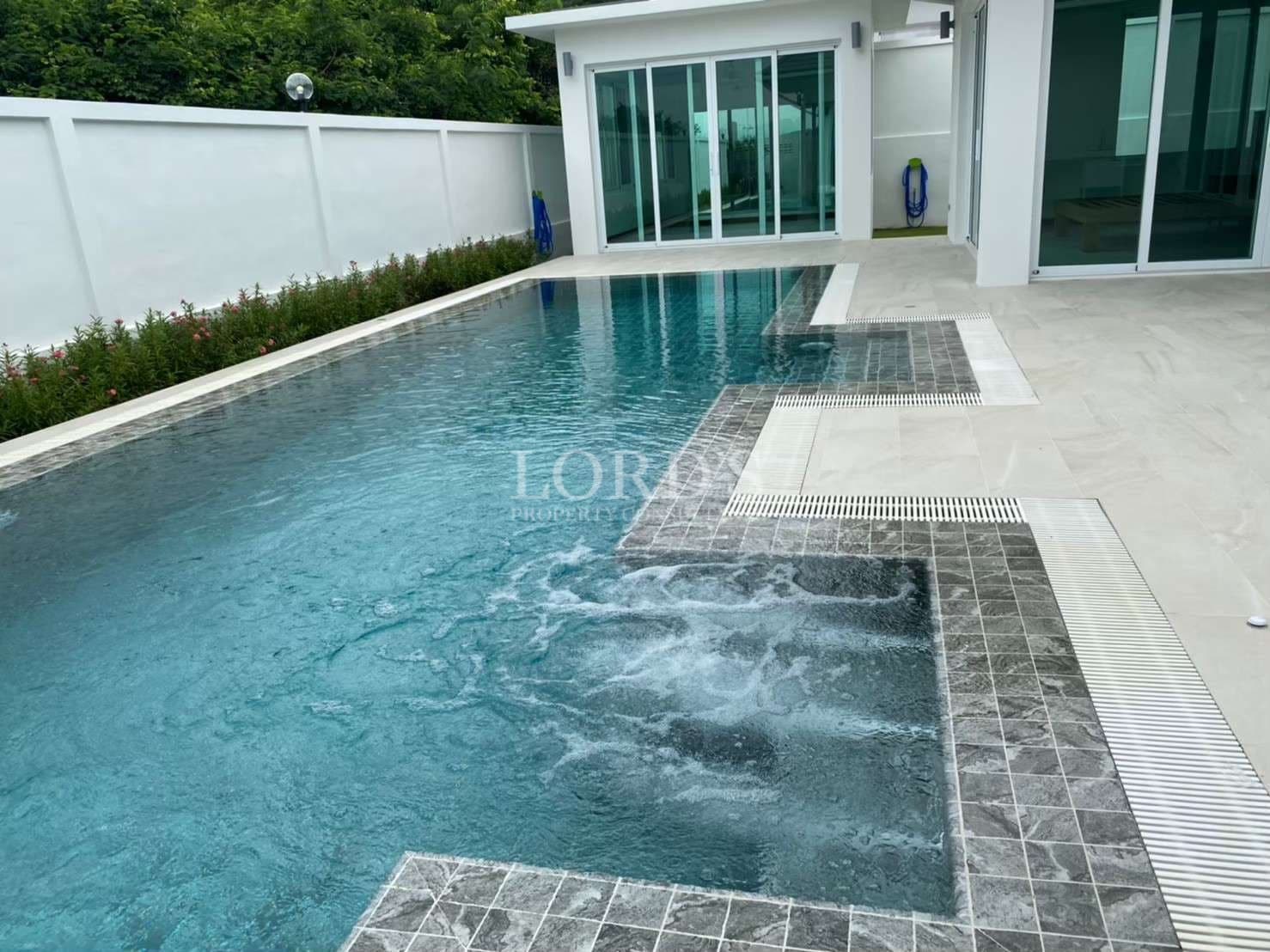 Private swimming pool with built-in jacuzzi, blue tiled water, and modern villa patio with sliding glass doors.