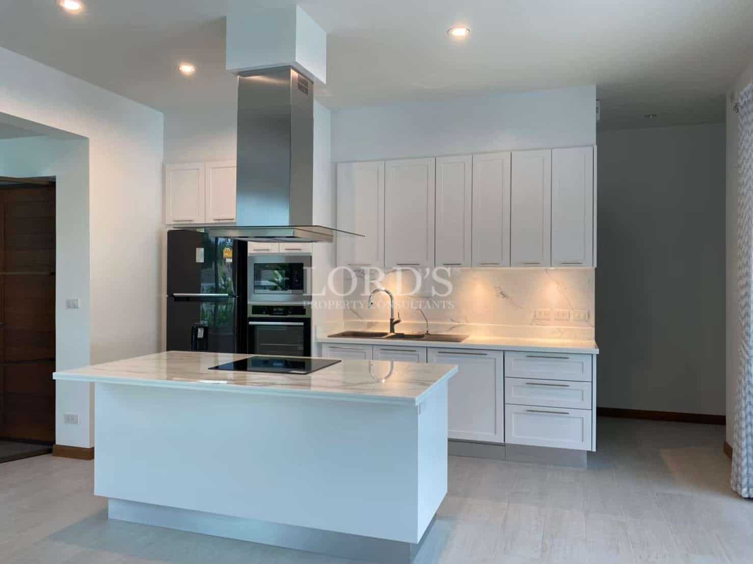 Modern white kitchen with marble-look island, built-in appliances, stainless steel range hood, and minimalist cabinetry.