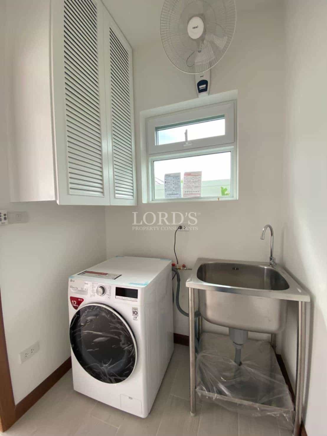 Compact laundry room with washing machine, stainless steel utility sink, wall cabinets, and ventilation window.