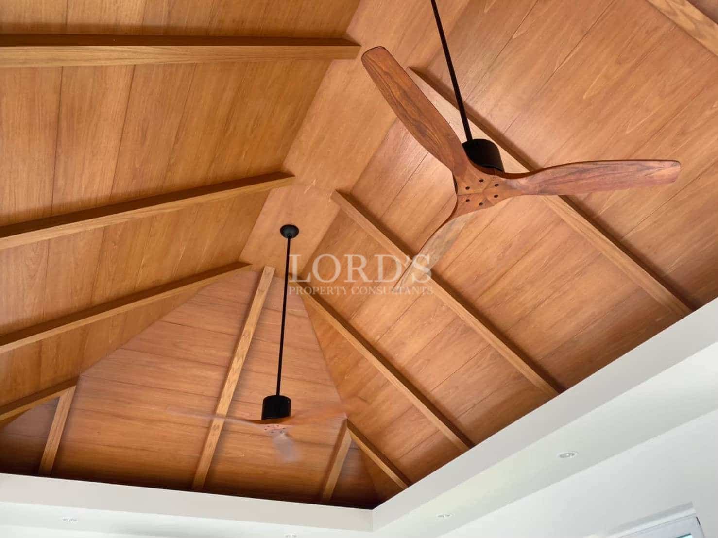 Vaulted wooden ceiling with exposed beams and modern ceiling fans in a luxury villa interior.