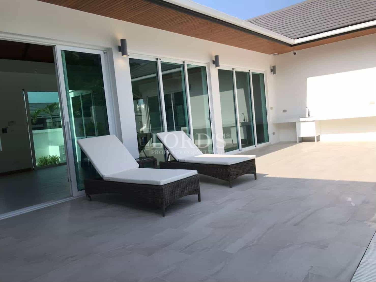 Modern poolside terrace with sun loungers, sliding glass doors, and a minimalist outdoor seating area.