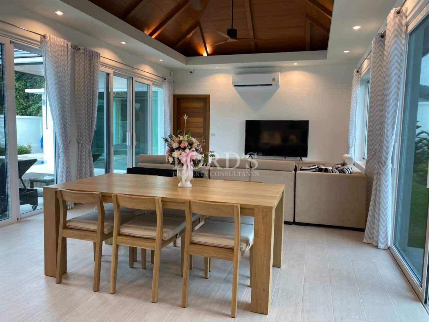 Modern open-plan living and dining area with wooden dining table, large windows, sliding glass doors, and a cozy lounge space.