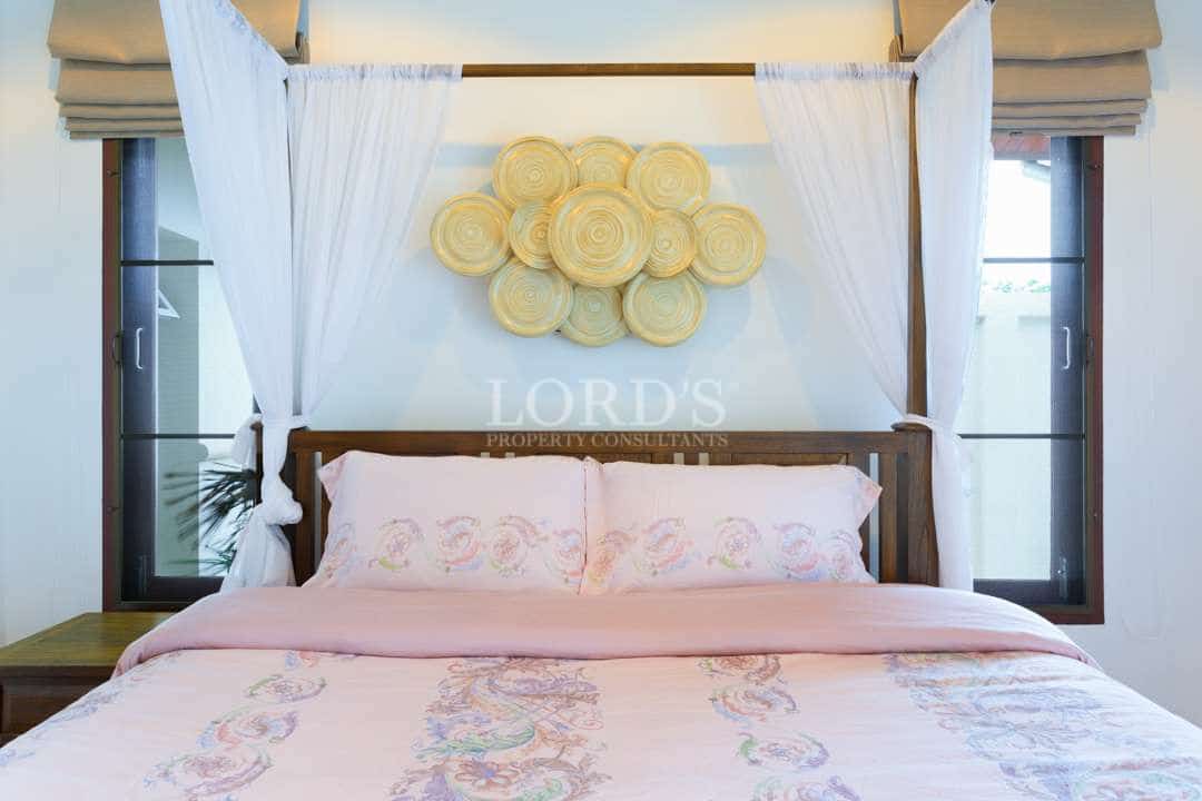Elegant four-poster bed with sheer white canopy curtains, soft pink patterned bedding, and decorative wall art in a bright bedroom.