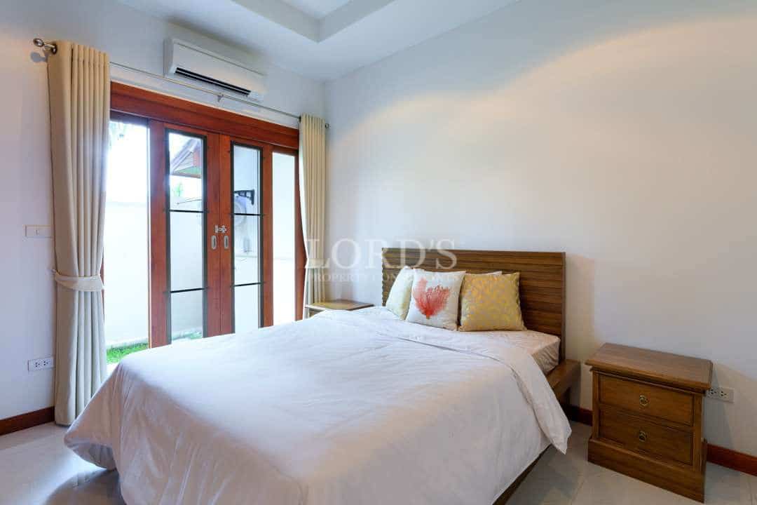 Modern bedroom with wooden bed frame, neutral bedding, bedside tables, and large glass doors opening to a private outdoor area.