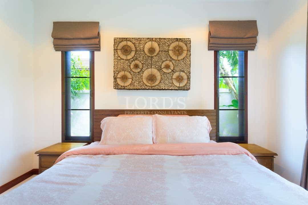 Symmetrical bedroom interior with a wooden bed, soft neutral bedding, decorative wall art, and tall windows bringing in natural light.