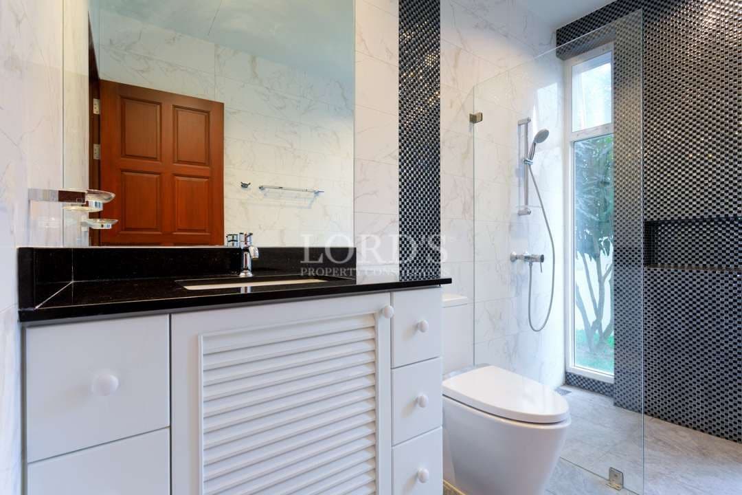 Modern bathroom interior with a white vanity, black countertop, glass-enclosed shower, rainfall showerhead, and natural light from a large window.