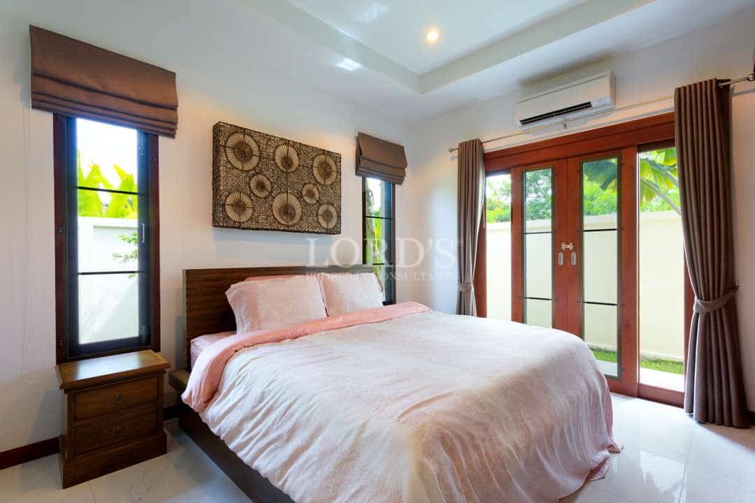 Bright modern bedroom with a wooden bed frame, soft neutral bedding, large glass doors, and natural light opening to a private garden.