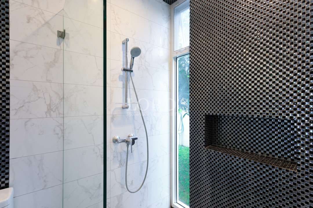 Modern walk-in shower with glass partition, marble-effect tiles, mosaic feature wall, and chrome rainfall shower fixtures