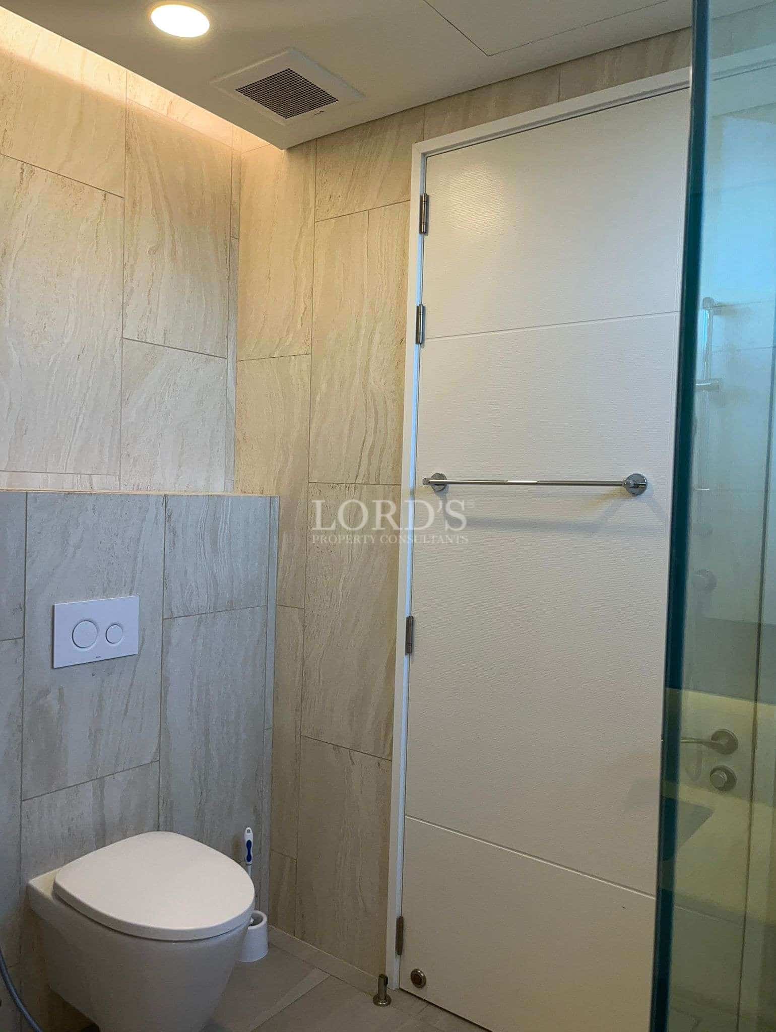 Modern bathroom with wall-mounted toilet, tiled walls, and glass shower partition