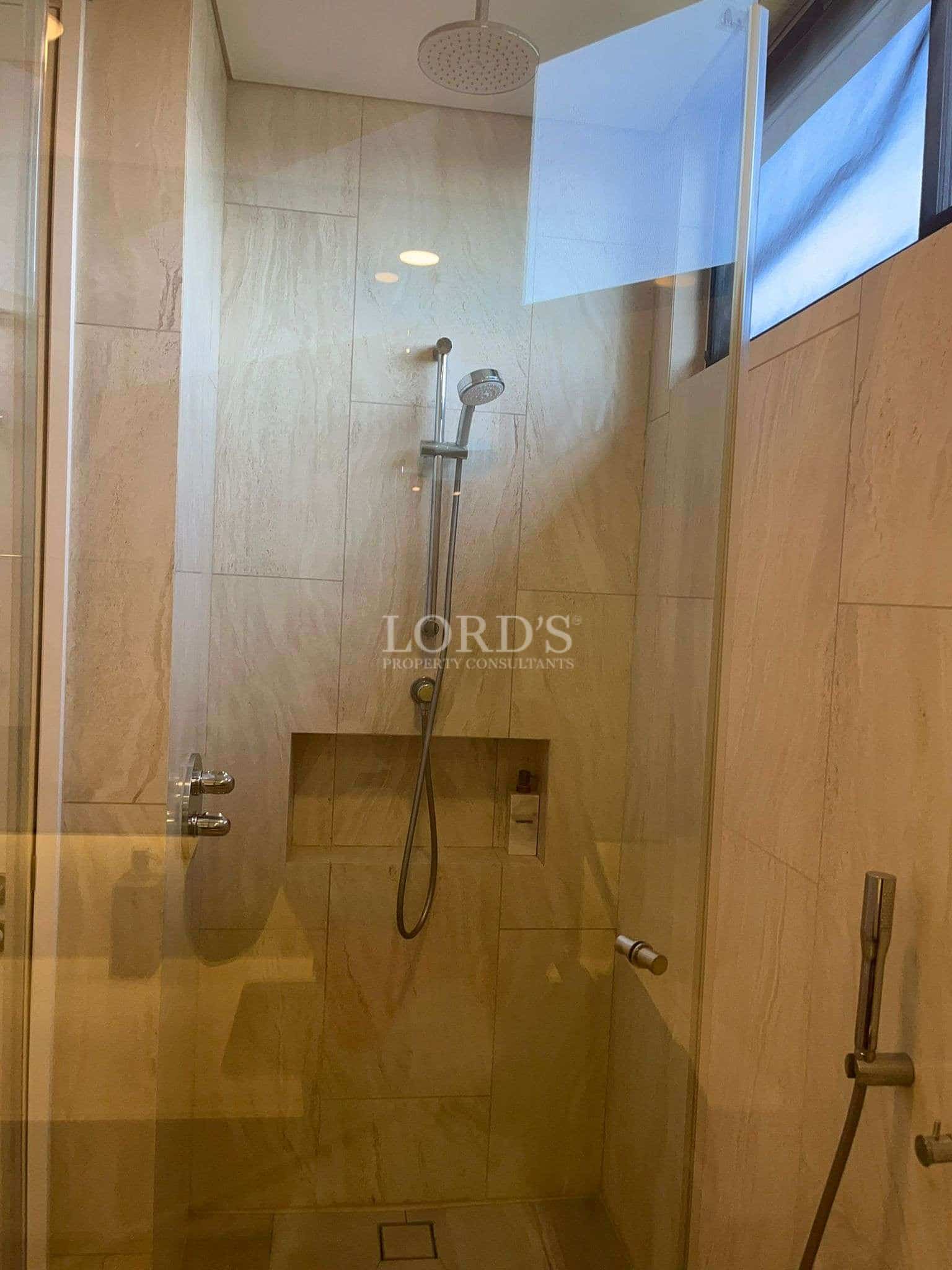 Modern walk-in shower with glass enclosure, rainfall showerhead, and beige stone tiles