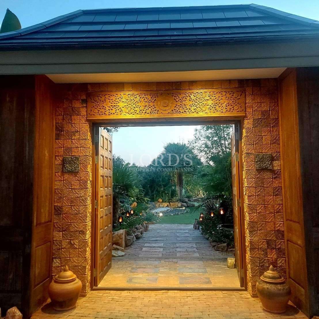 Traditional carved wooden entrance gate leading into a landscaped tropical garden at a luxury villa estate.