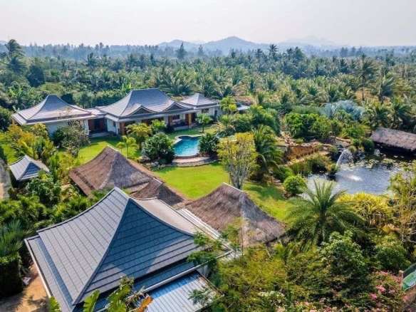 Aerial view of a luxury villa estate surrounded by palm trees, landscaped gardens, swimming pool, and natural pond.