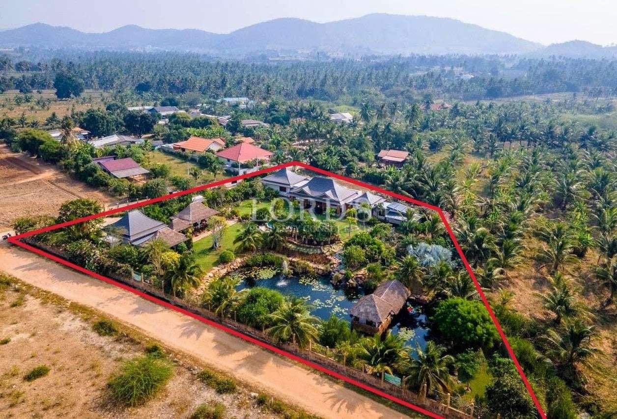 Aerial view of a large private property with villas, landscaped gardens, pond, and clearly marked land boundaries.
