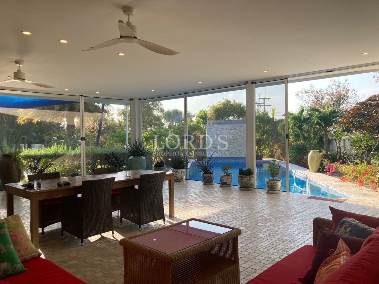 Covered outdoor living and dining area with ceiling fans, floor-to-ceiling glass doors, and swimming pool views.