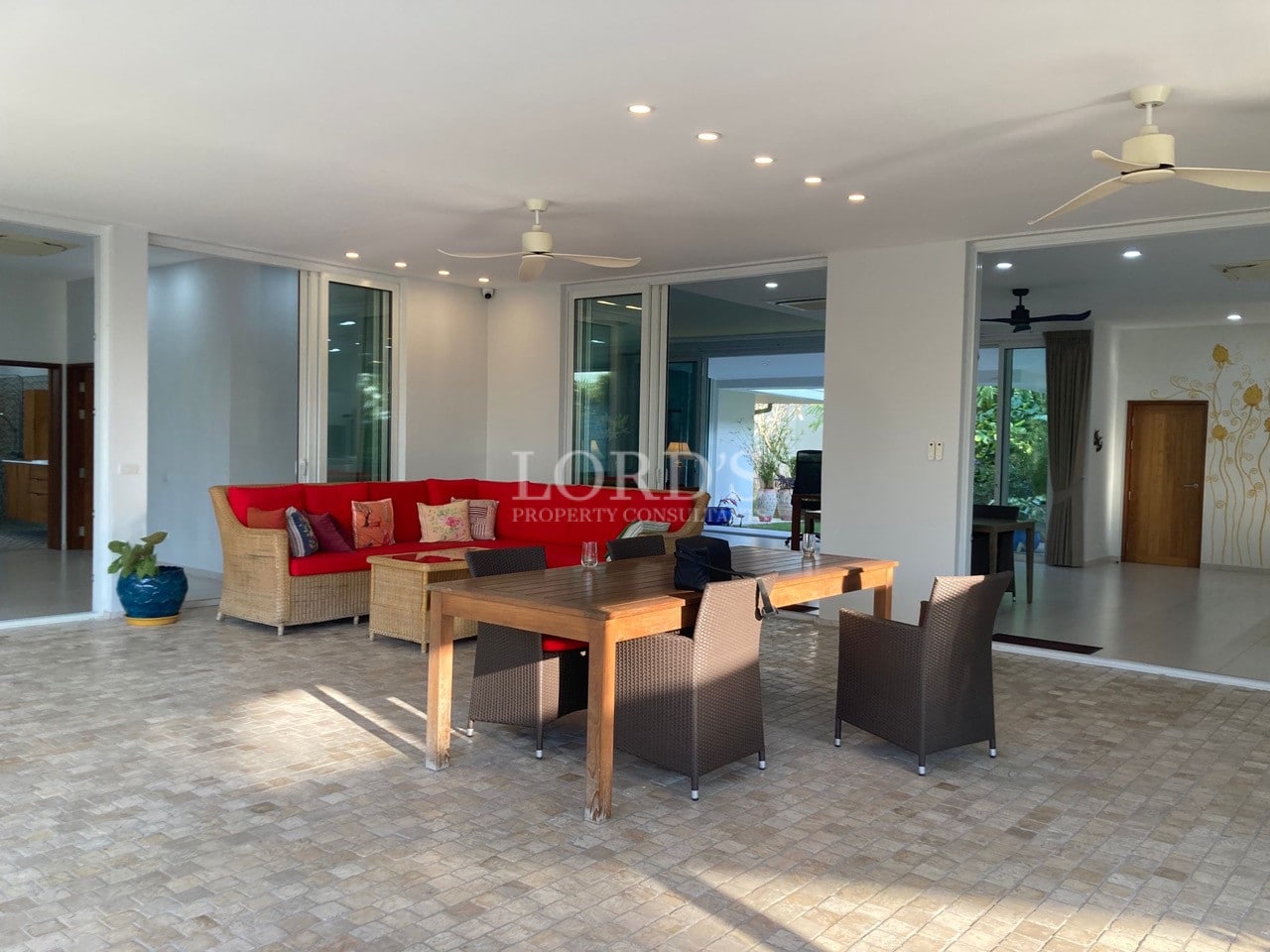 Spacious covered outdoor living and dining area with modern furniture, ceiling fans, and garden views.