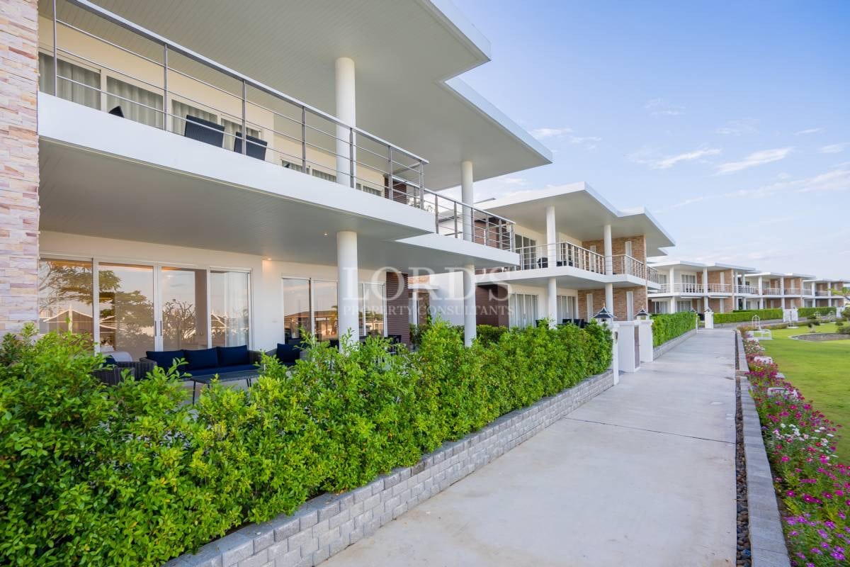 Modern residential villas with covered terraces, balconies, landscaped hedges, and pedestrian walkway.