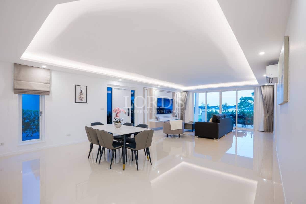 Spacious open-plan living and dining area with modern furniture, recessed ceiling lighting, and large windows.