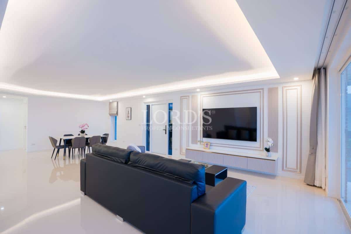 Spacious open-plan living and dining area with feature TV wall, recessed ceiling lighting, and modern furnishings.