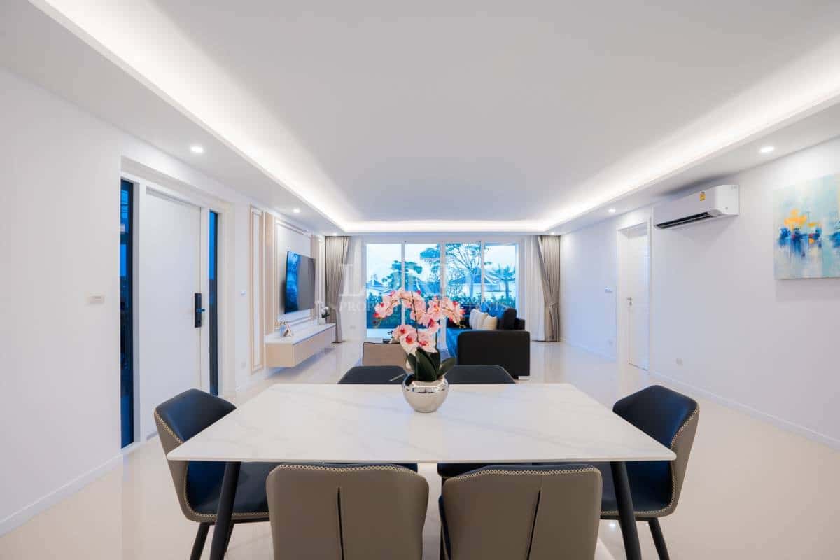 Open-plan living and dining area with modern furniture, recessed ceiling lighting, and large windows.