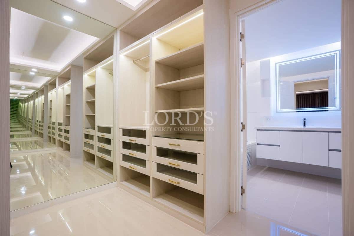 Spacious walk-in wardrobe with custom shelving, drawers, full-height mirrors, and ensuite bathroom access.