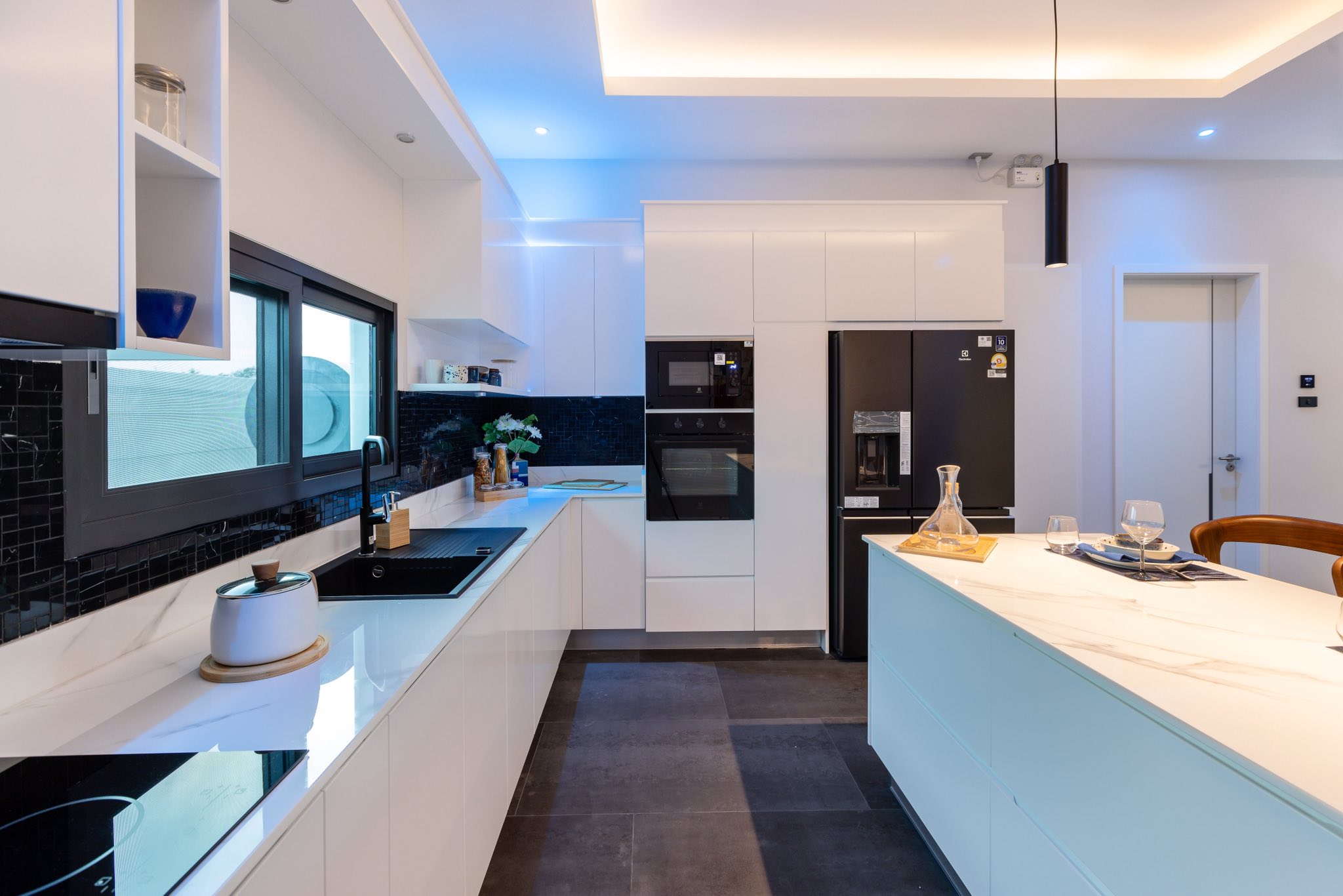 Modern white kitchen with marble island, black appliances, and ambient ceiling lighting.