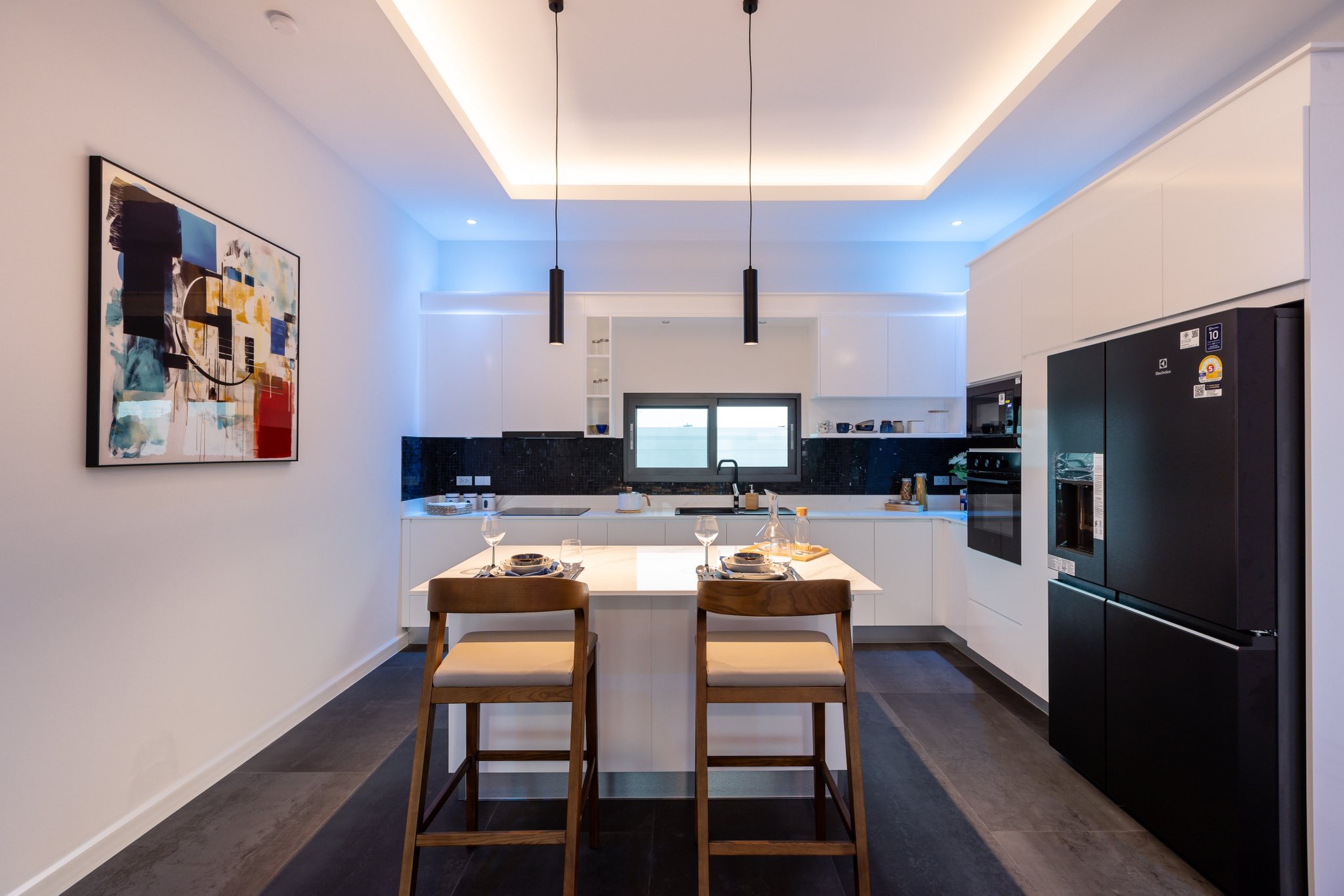 Modern white kitchen with island seating, pendant lights, and built-in black appliances.