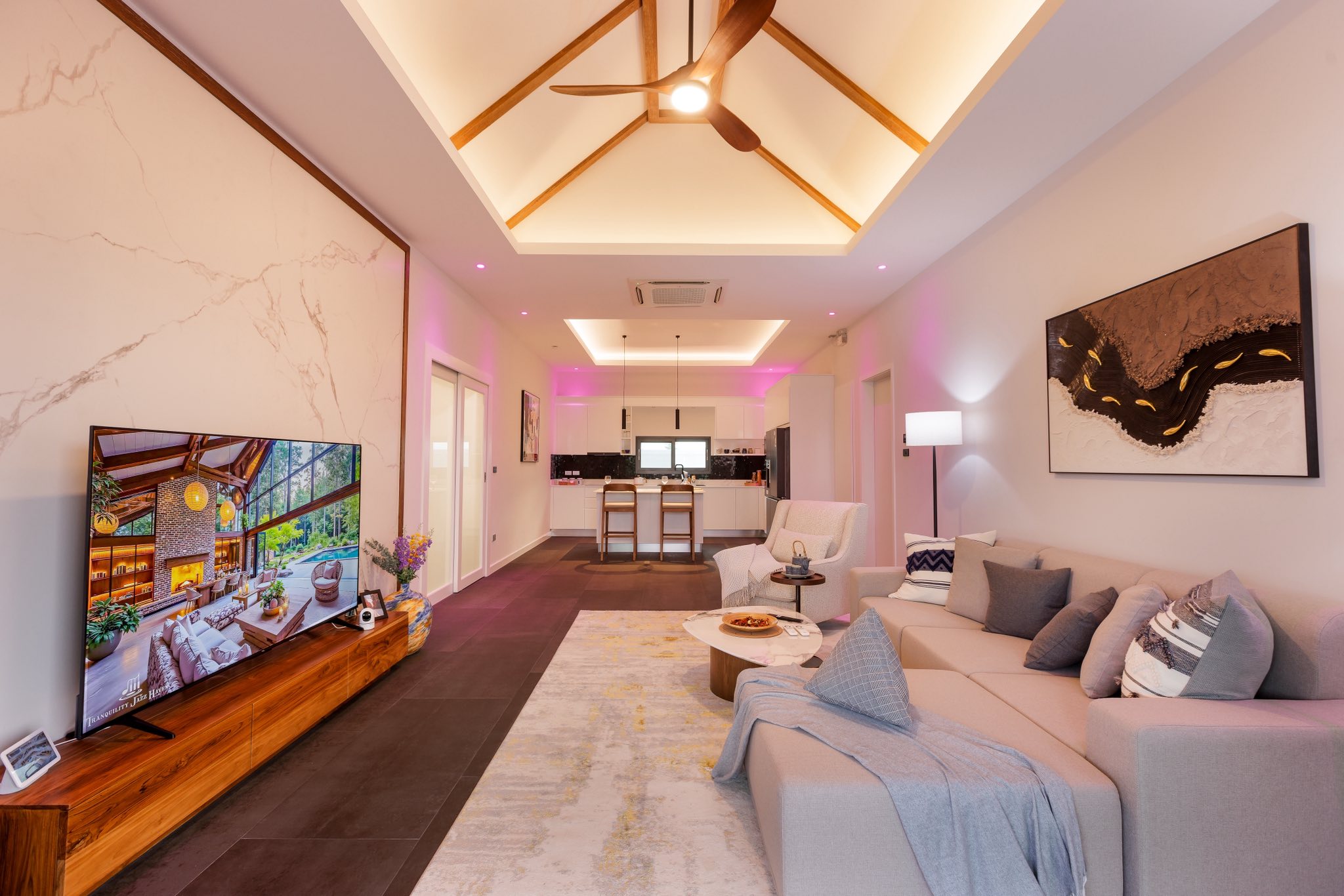 Modern open-plan living room with vaulted ceiling, ceiling fan, ambient LED lighting, and kitchen view.