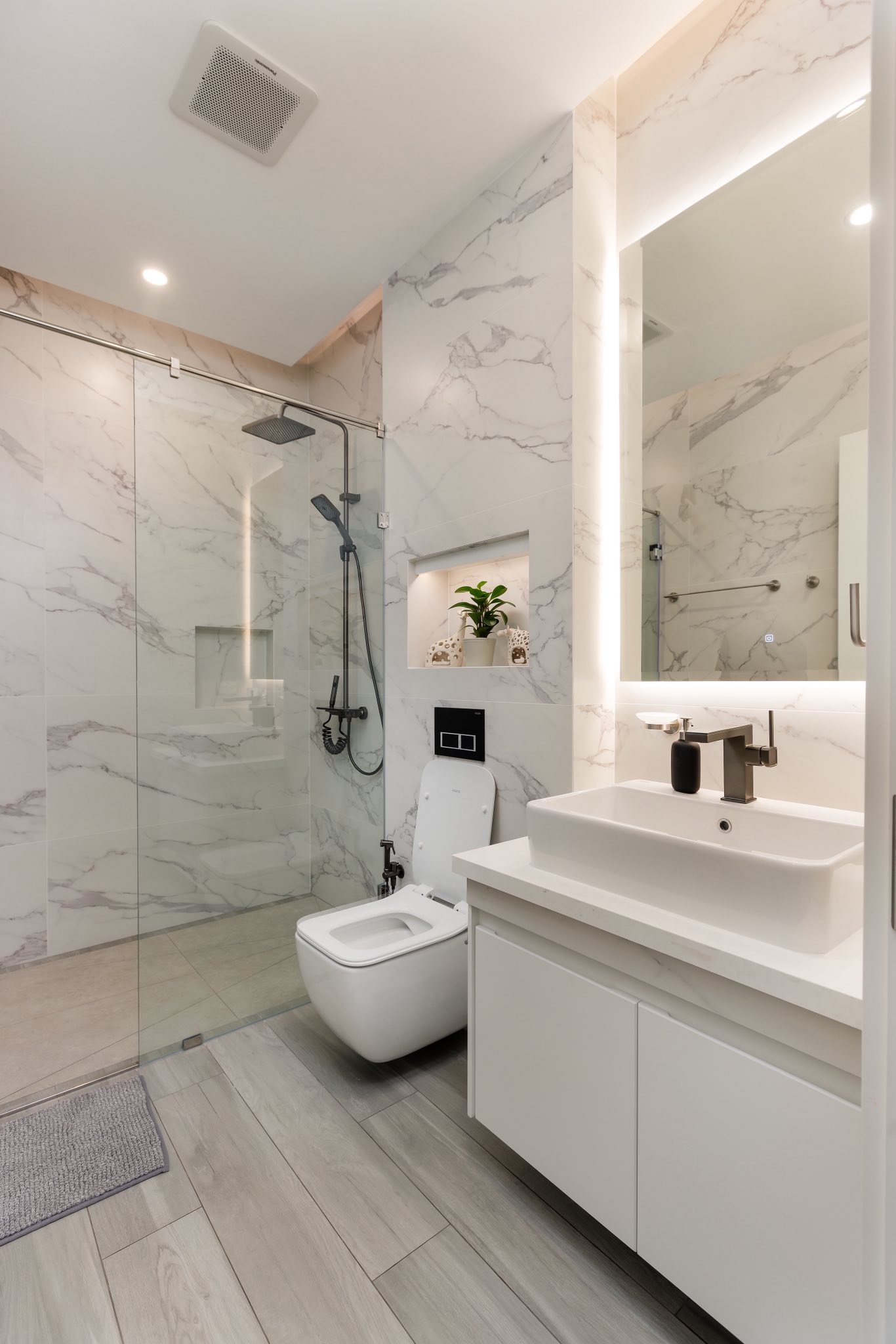 Modern marble bathroom with glass shower, wall-mounted toilet, and vanity sink.