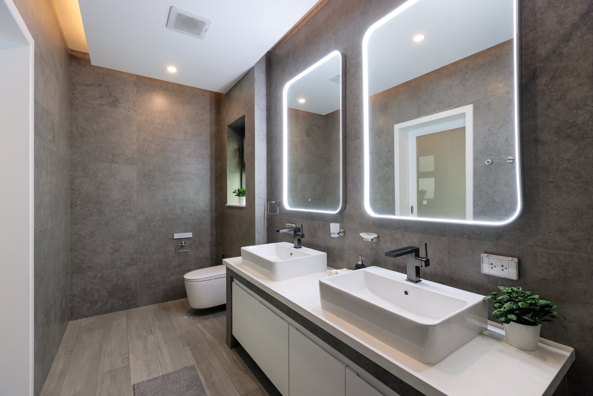 Modern bathroom with double vanity sinks, LED backlit mirrors, and gray stone tiles.