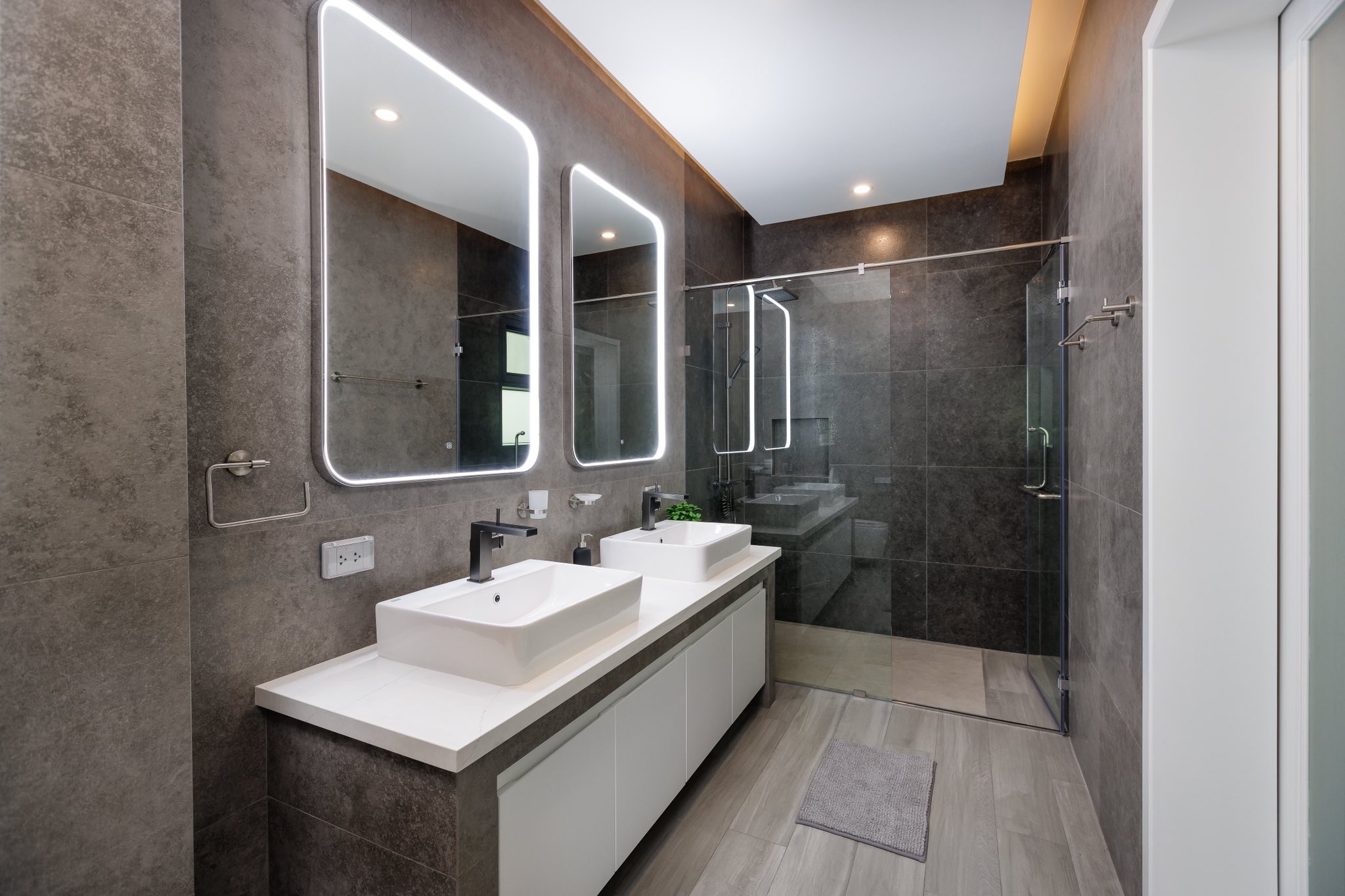Modern luxury bathroom with double sink vanity, illuminated mirrors, and glass shower enclosure.