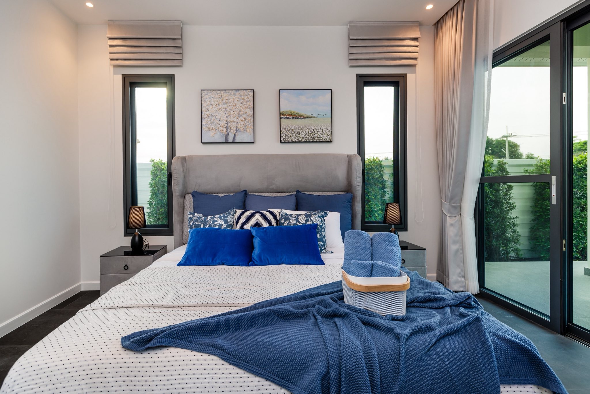 Modern bedroom with blue accents, comfortable bed, soft lighting, and large windows.