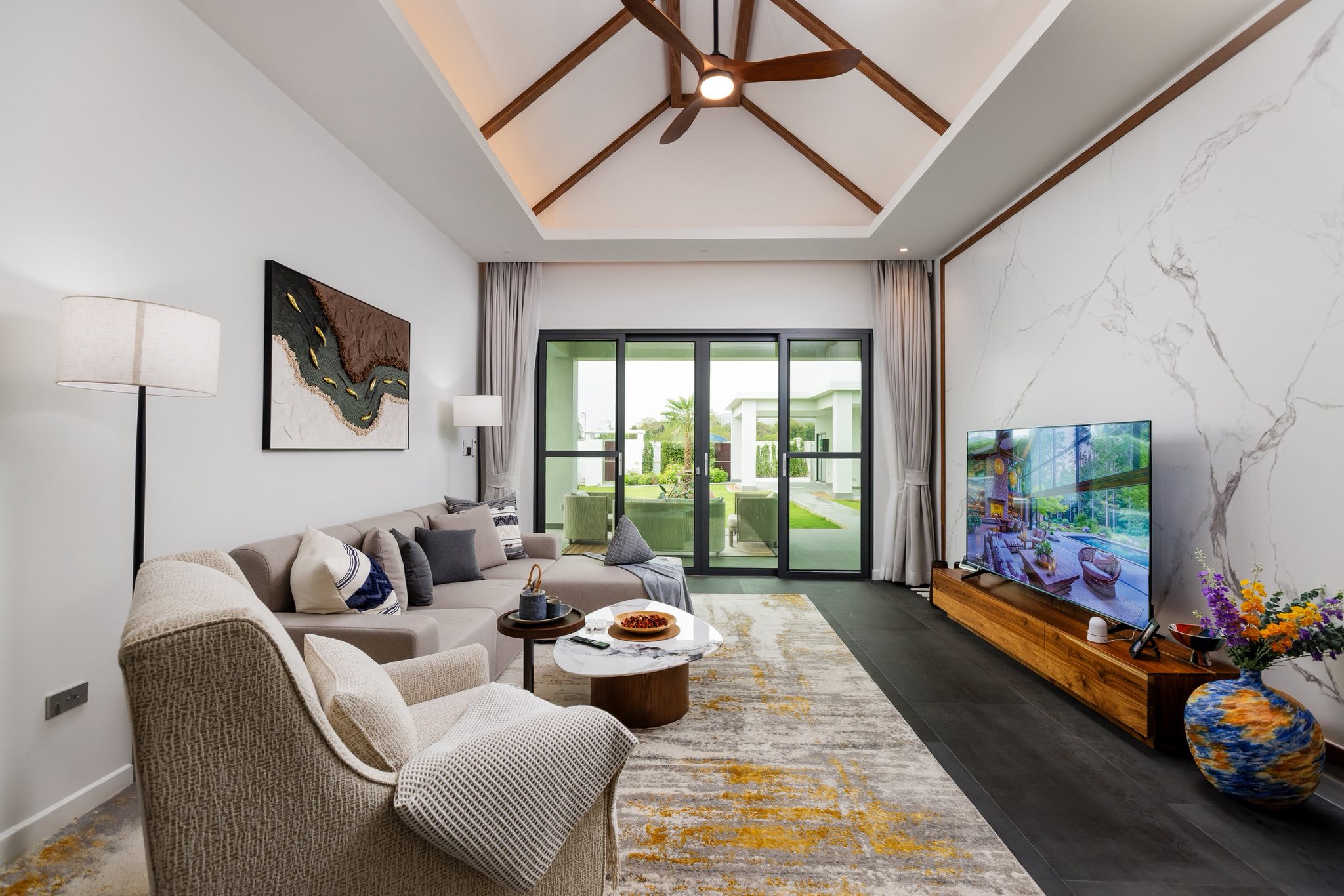 Modern living room with high ceiling, wooden roof accents, comfortable seating, and large glass sliding doors.