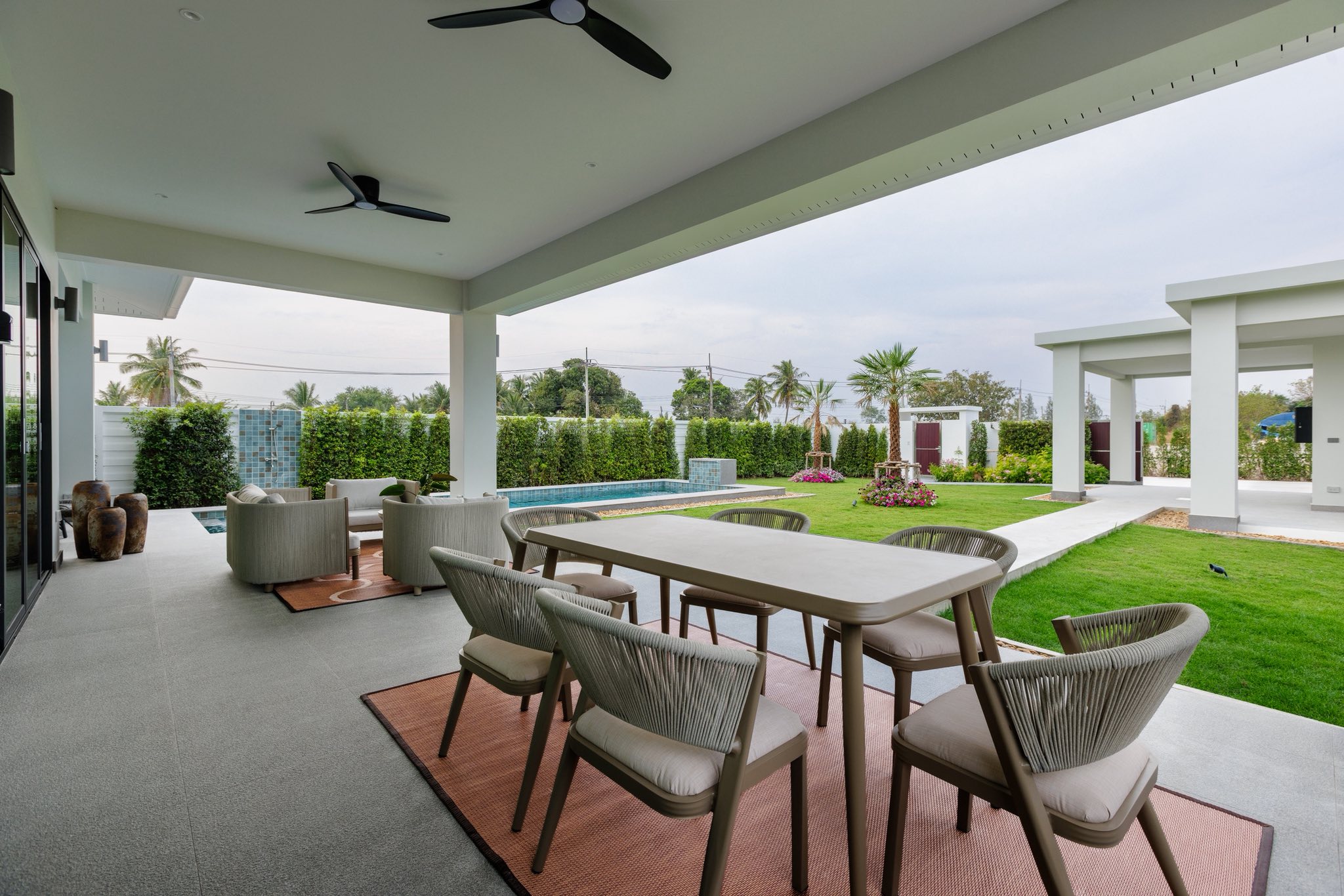 Covered outdoor dining and lounge area with modern furniture, garden view, and private pool.