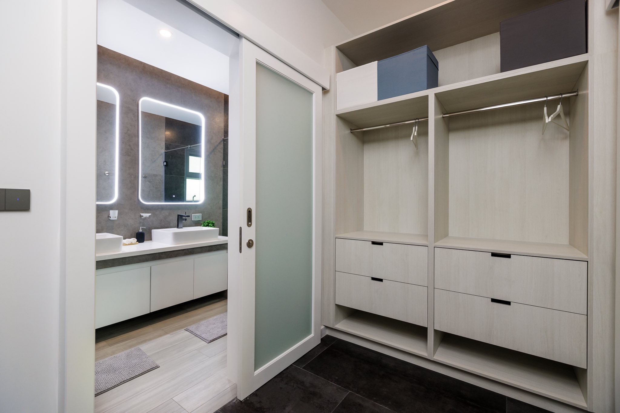 Modern walk-in closet with built-in storage and sliding door leading to a contemporary bathroom.
