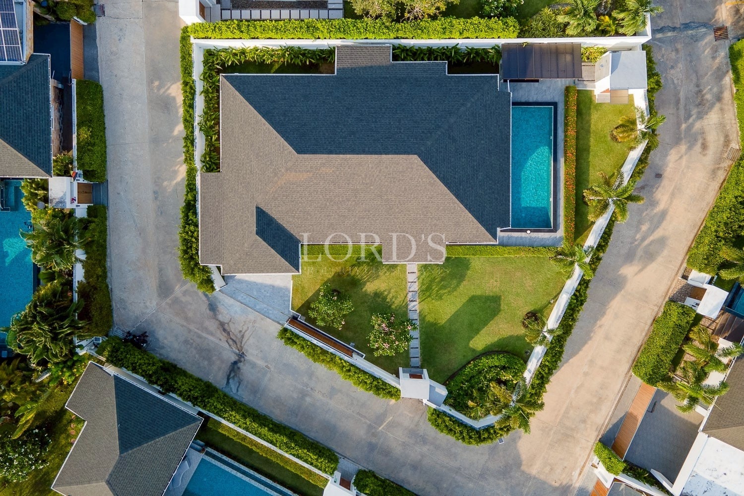 Aerial view of a modern residential villa with a private swimming pool, landscaped garden, and surrounding streets.