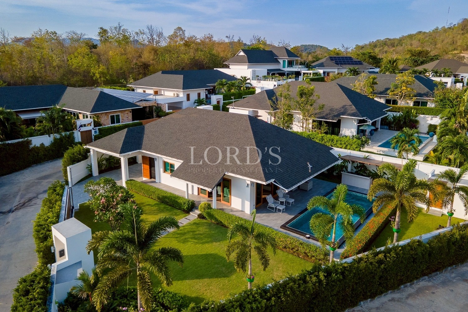 Aerial view of a modern luxury villa with private swimming pool, landscaped garden, and surrounding upscale homes.