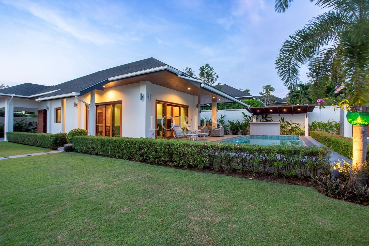 Modern single-story luxury villa with private swimming pool, landscaped garden, and outdoor seating area at sunset.