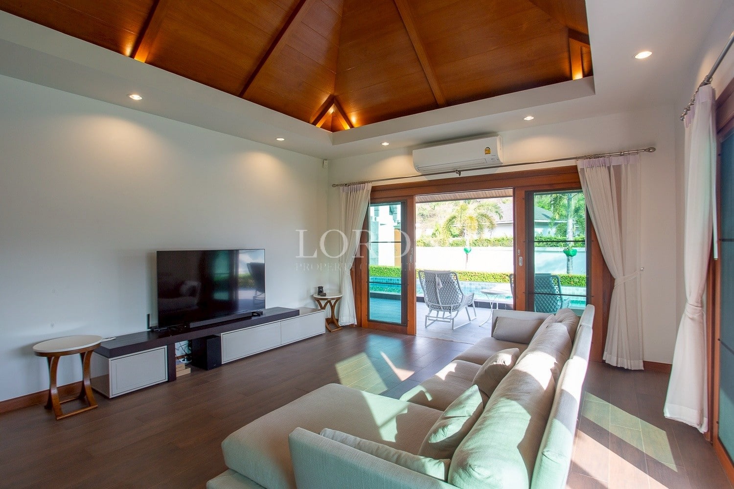 Modern living room with wooden ceiling, large sofa, and sliding glass doors to pool