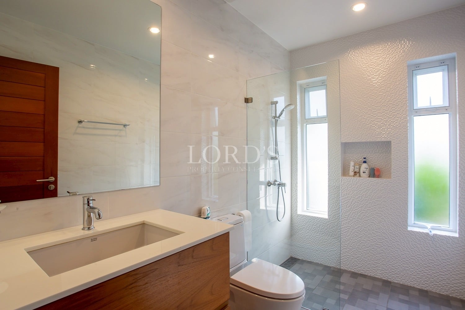 Modern bathroom with glass shower, wooden vanity, and natural light