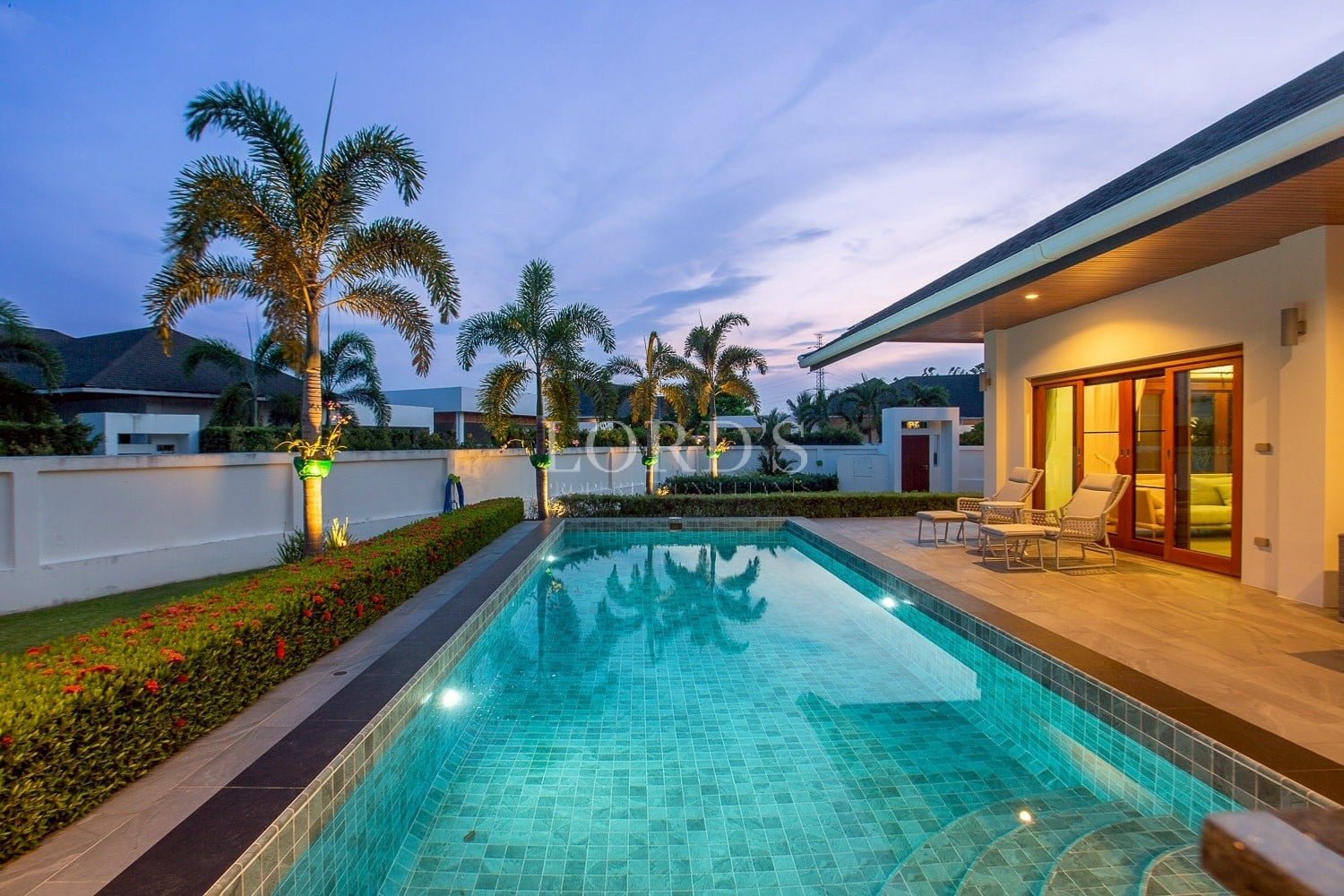 Private villa swimming pool at dusk with palm trees and outdoor seating