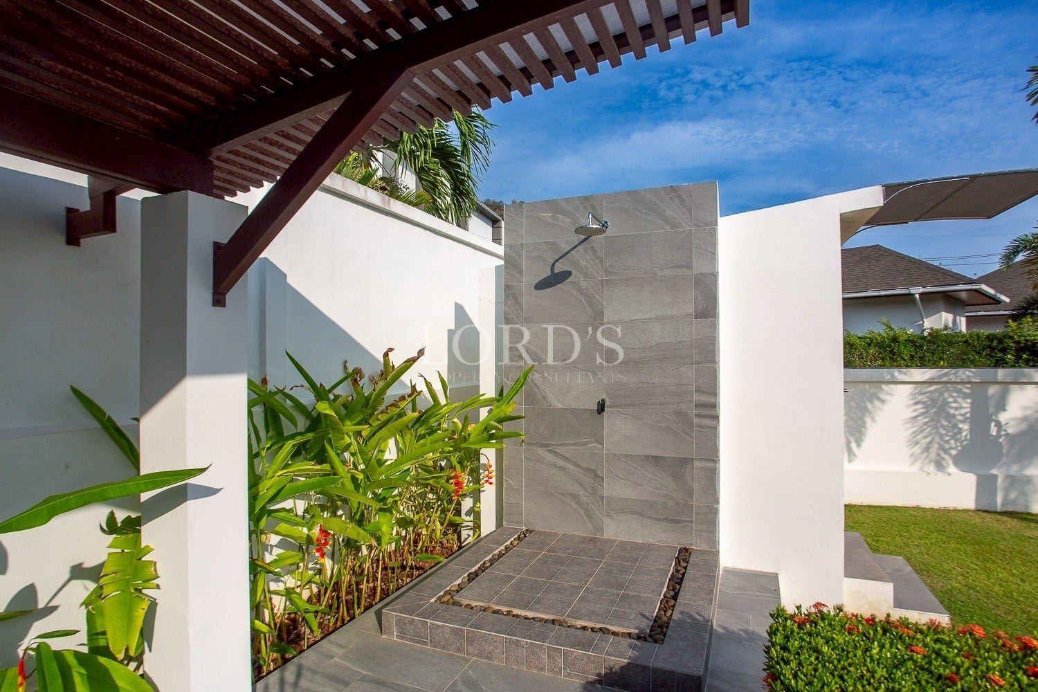 Outdoor garden shower with modern stone wall, tropical plants, and open-air design