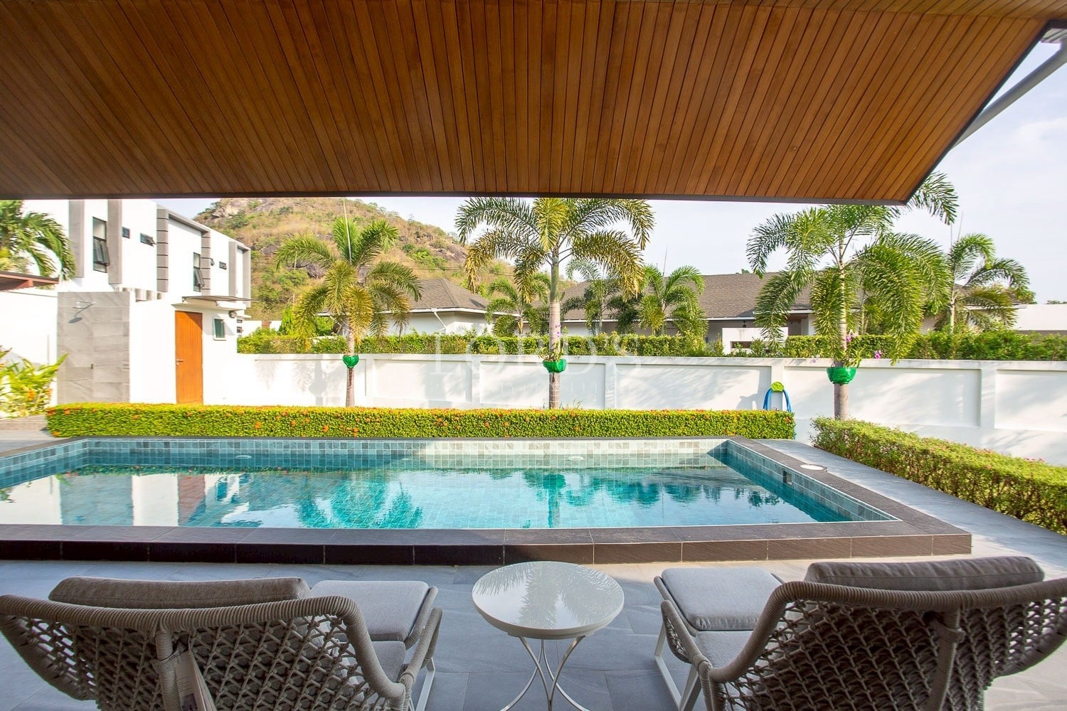 Covered outdoor seating area overlooking a private swimming pool with palm trees