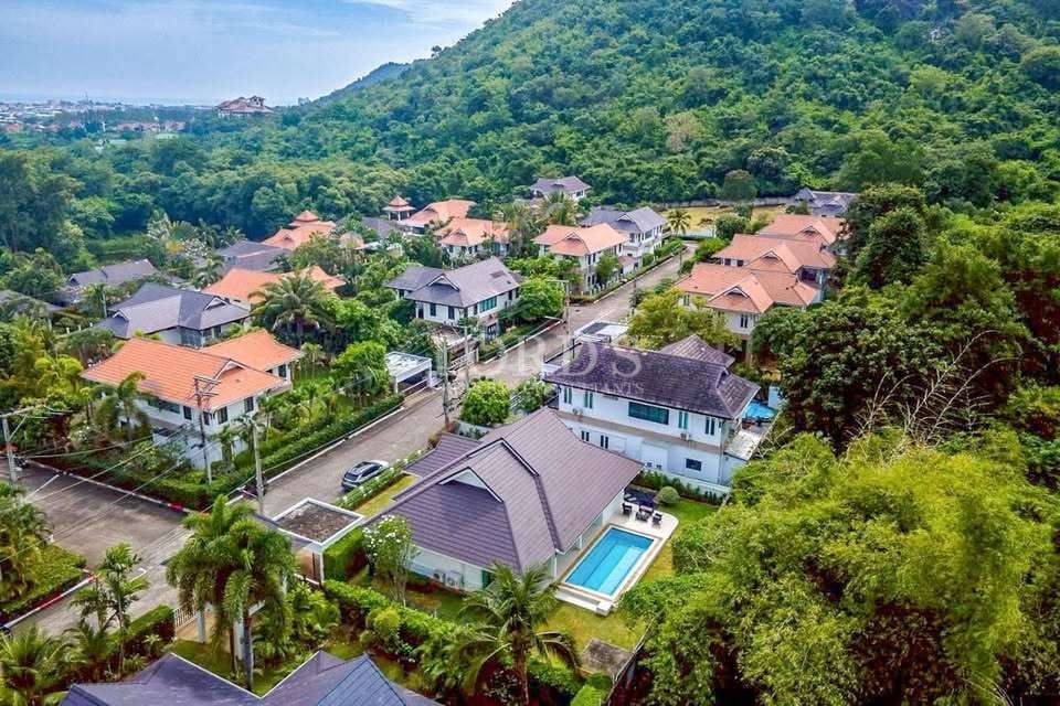 Aerial view of a luxury residential neighborhood with tropical villas, private pools, and lush green hillside surroundings