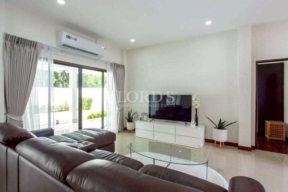 Modern living room with leather sofa, glass coffee table, wall-mounted TV, sliding glass doors, and air conditioning