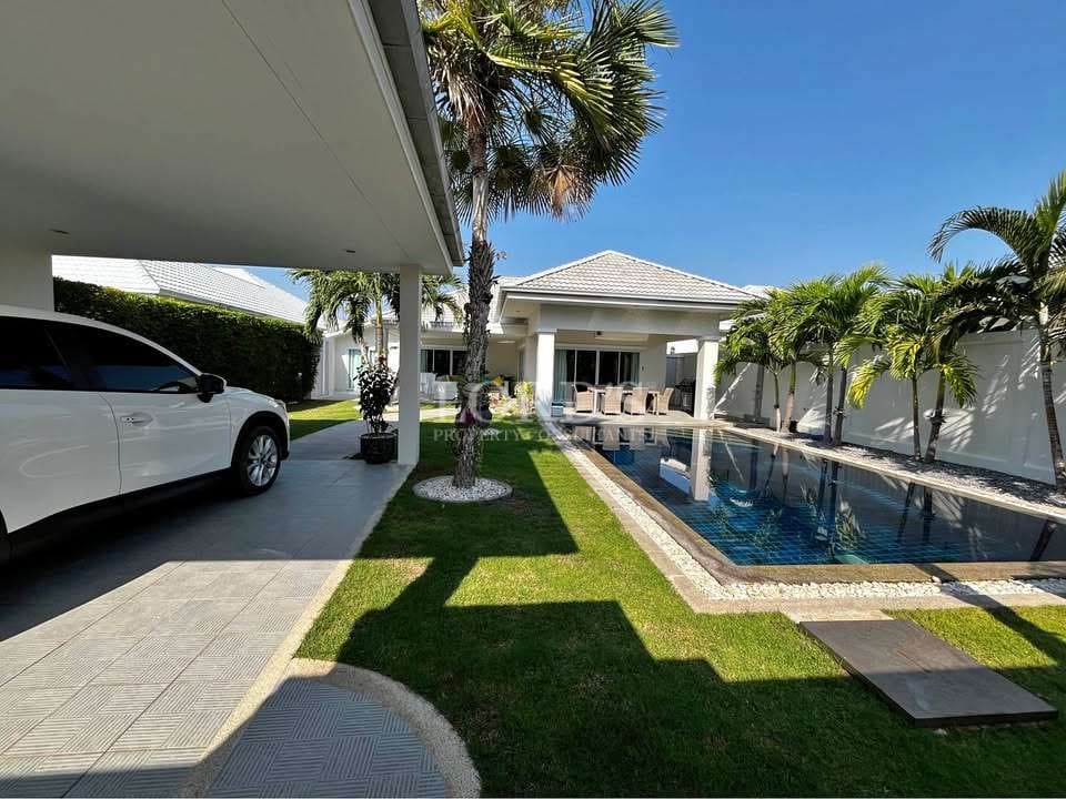 Luxury villa exterior with private swimming pool, covered carport, palm trees, and manicured lawn under clear blue sky