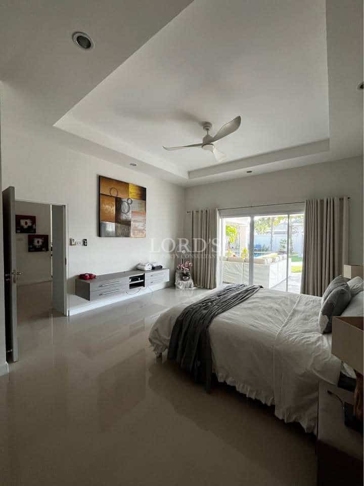 Spacious modern bedroom with king-size bed, ceiling fan, glossy tiled floor, sliding glass doors, and garden view