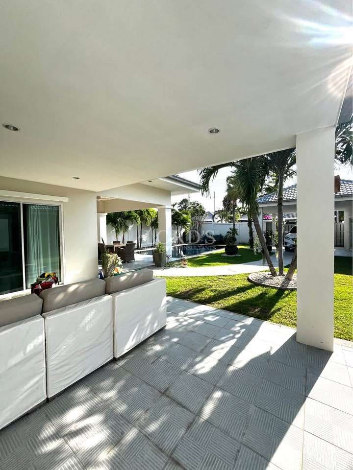 Covered outdoor patio with seating area, tiled floor, landscaped garden, palm trees, and natural sunlight